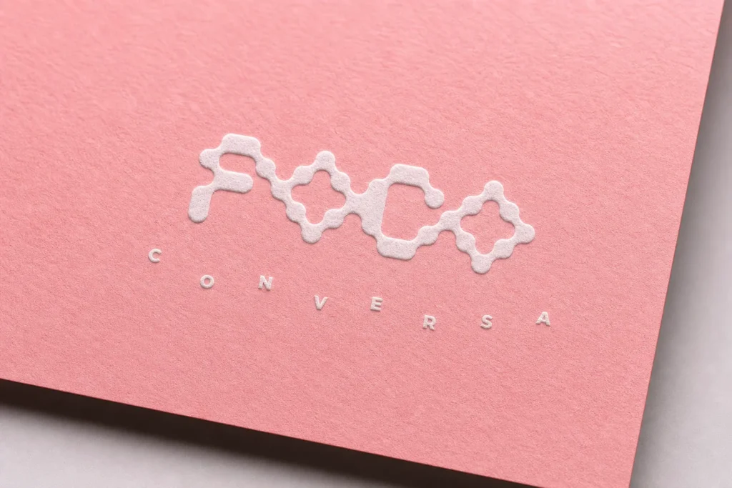 Logotipo en bajorrelieve de Foco Abierto Conversa sobre papel de algodón rosa, diseñado por Creatias Estudio