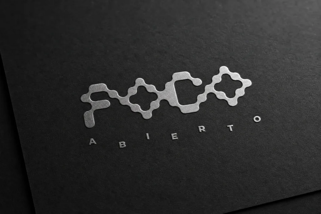 Logotipo en bajorrelieve plateado de Foco Abierto sobre papel negro, diseñado por Creatias Estudio