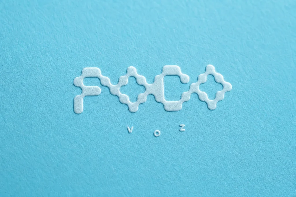 Logotipo en bajorrelieve de Foco Abierto Voz sobre papel de algodón azul, diseñado por Creatias Estudio